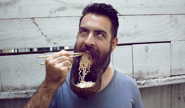 man eating noodles out of his beard with chopsticks